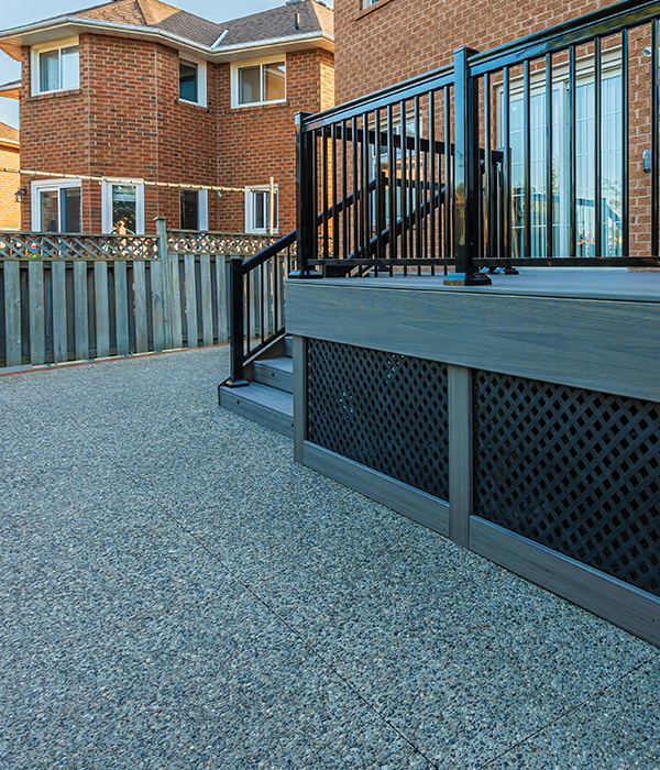 Durable outdoor epoxy flake flooring installed on a residential patio area near a backyard deck.